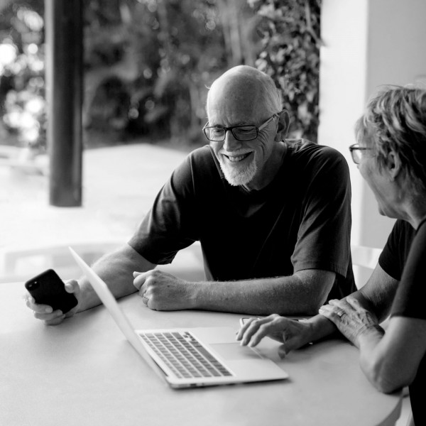 Älteres Ehepaar sitzt gut gelaunt vor einem Laptop auf einer Terasse